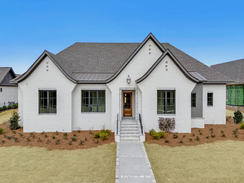 White home with curved front gables, dark roof and steps to a wood front door