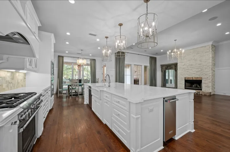White kitchen island with pendant lights beside a living room with a brick fireplace