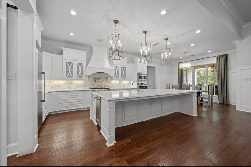 Wide view of a white kitchen with a large island and wood floors