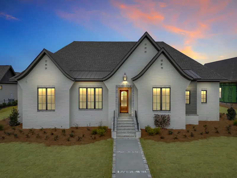 White gabled home with illuminated windows beneath a sunset sky
