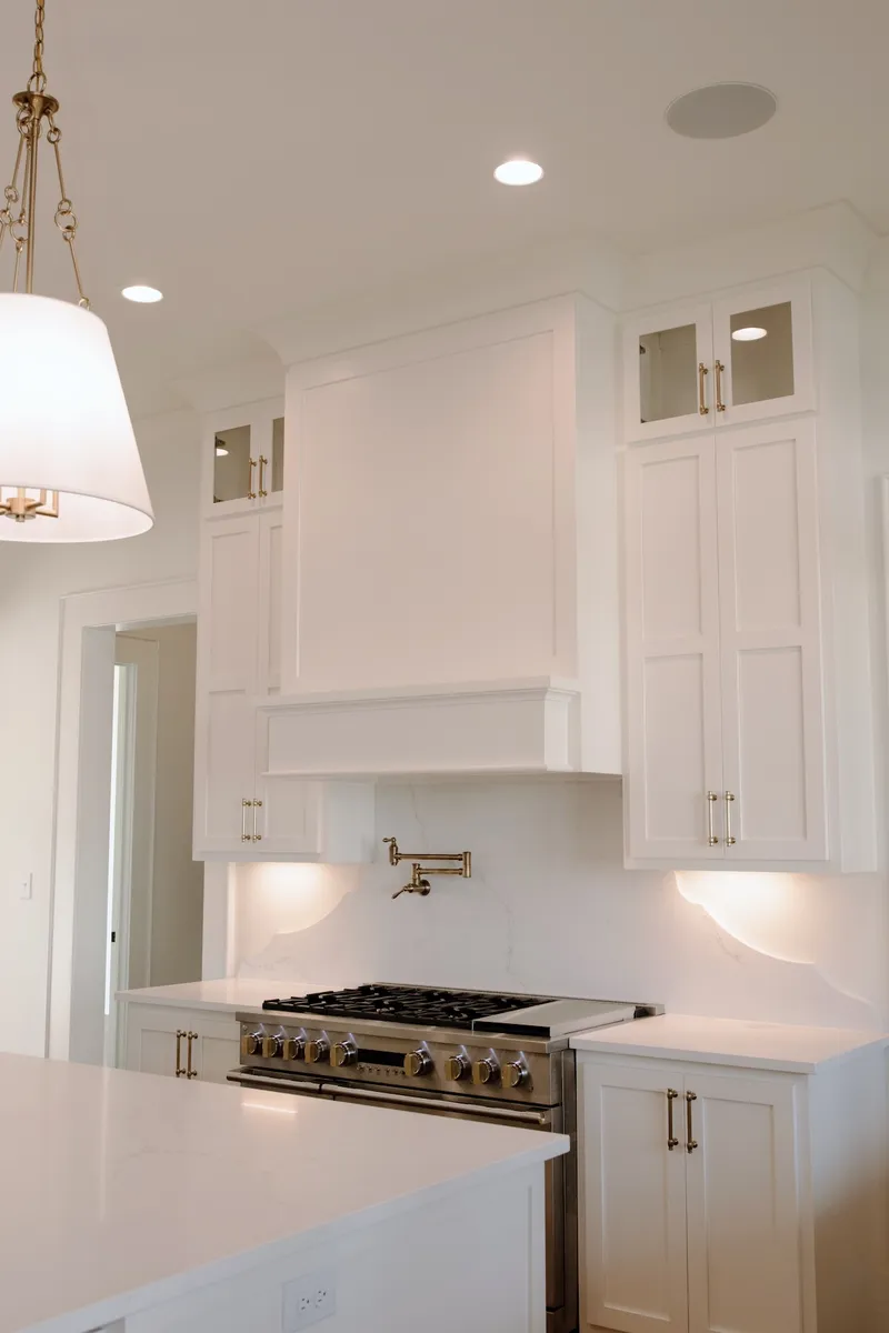 Kitchen range beneath a white vent hood and upper cabinets