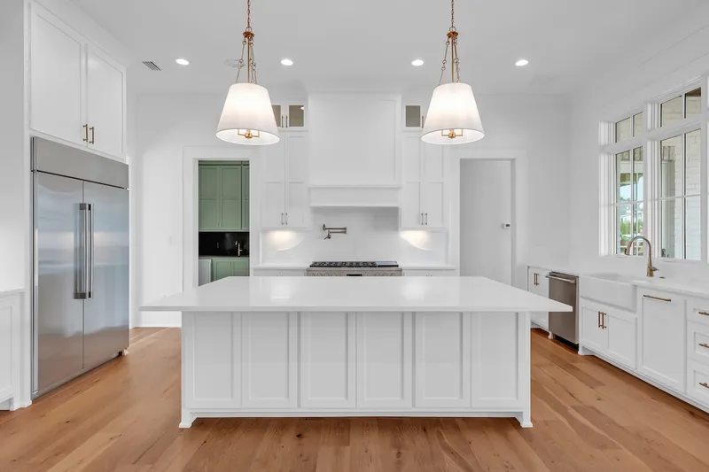 White kitchen island with two pendant lights and a stainless refrigerator