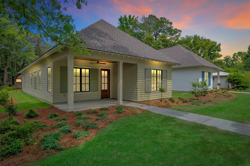 Cottage with a wraparound porch and illuminated windows at dusk