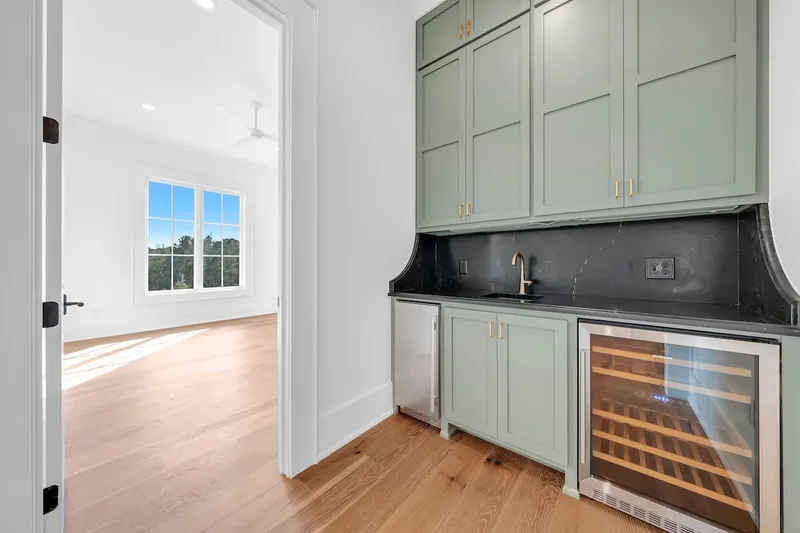 Green built-in beverage cabinet with a sink and glass-front refrigerator