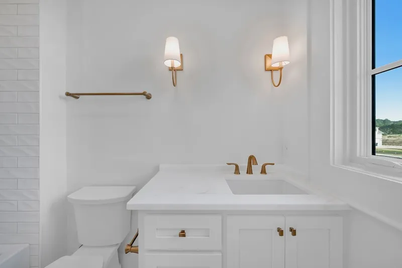 Compact bathroom with a white vanity, window and brass-colored wall light