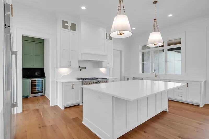 White kitchen island with pendant lights and an adjacent green beverage cabinet