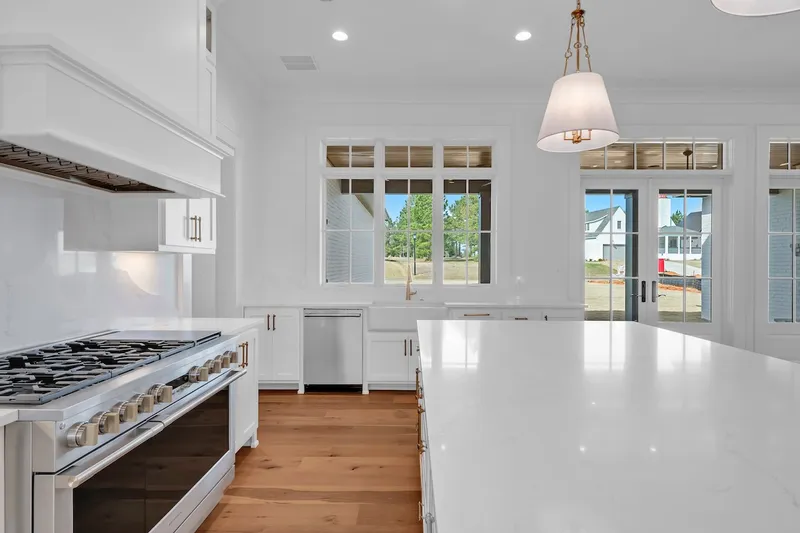 White kitchen with a gas range, long island and windows along the rear wall