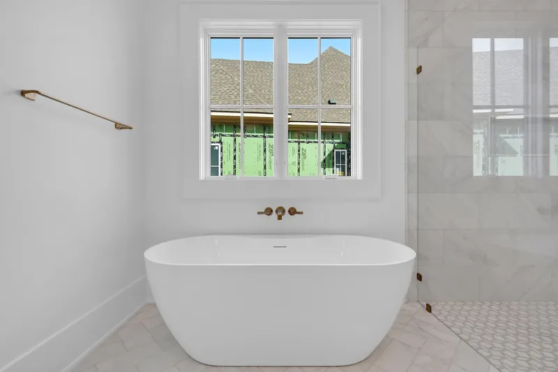 Freestanding white bathtub below a window beside a glass shower enclosure