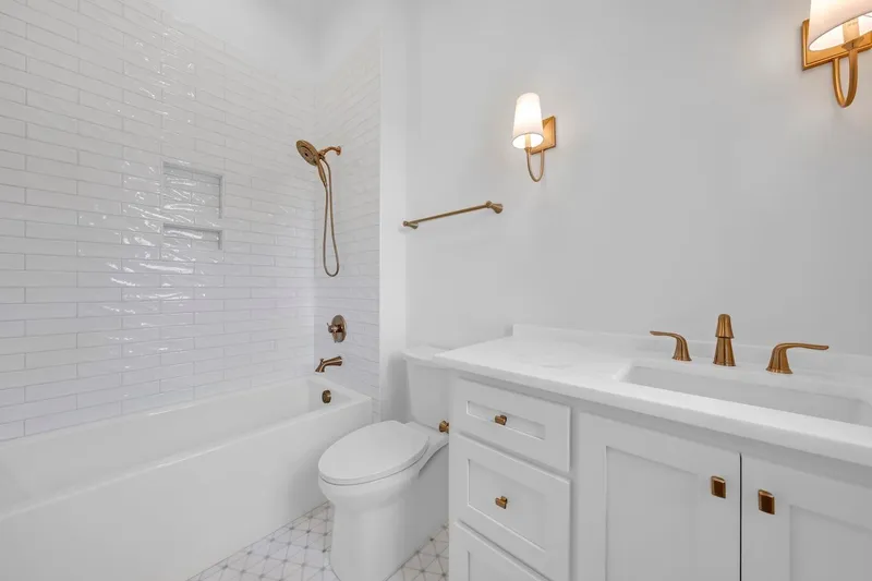 Bathroom with a tiled tub surround, white vanity and brass-colored fixtures