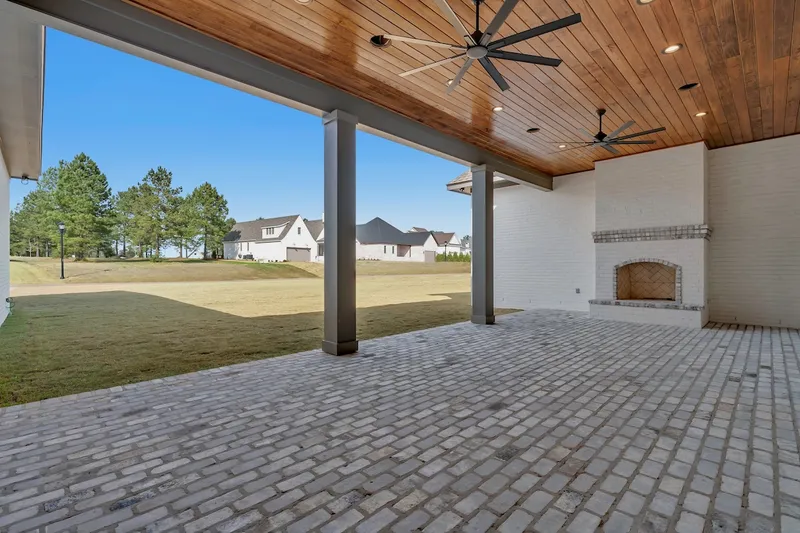 Covered rear porch with a wood ceiling, ceiling fans and fireplace overlooking a lawn