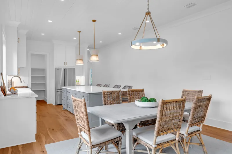 Dining table beside a white kitchen island with woven barstools